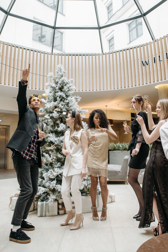 Group of diverse adults celebrating a festive Christmas party indoors with a decorated Christmas tree.
